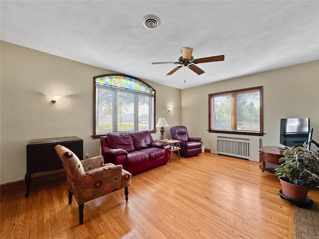 living room featuring radiator heating unit, light wood-type flooring, and ceiling fan