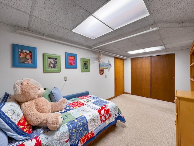 carpeted bedroom featuring a closet and a drop ceiling