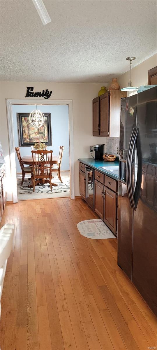 kitchen with light hardwood / wood-style floors, a textured ceiling, hanging light fixtures, and black fridge with ice dispenser