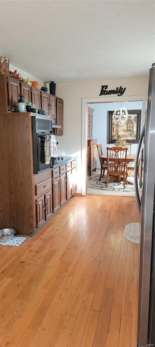 kitchen featuring stainless steel fridge, a textured ceiling, light hardwood / wood-style floors, and oven