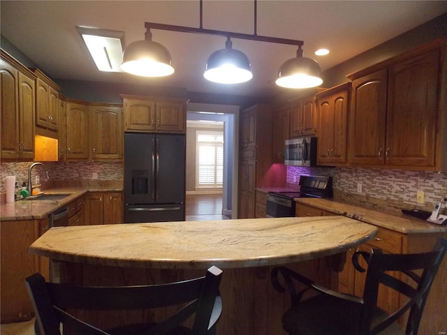 kitchen with a kitchen bar, black appliances, sink, tasteful backsplash, and decorative light fixtures