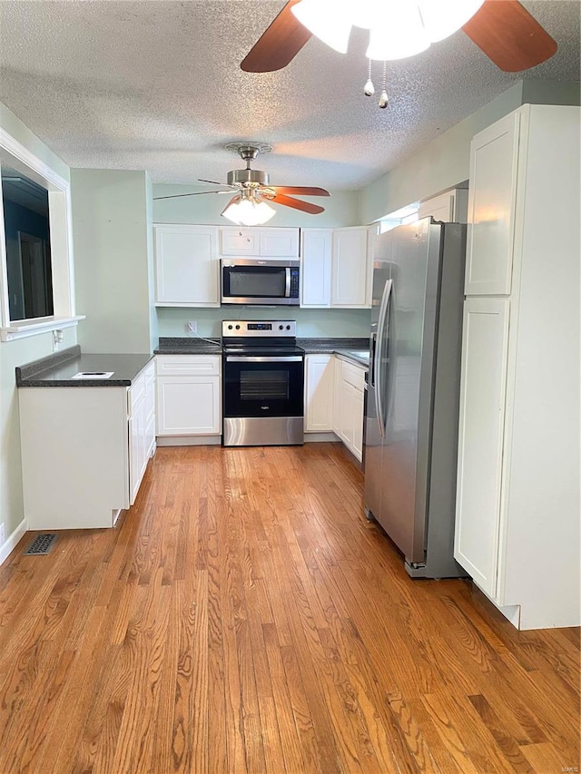 kitchen with appliances with stainless steel finishes, light hardwood / wood-style flooring, white cabinets, and a textured ceiling