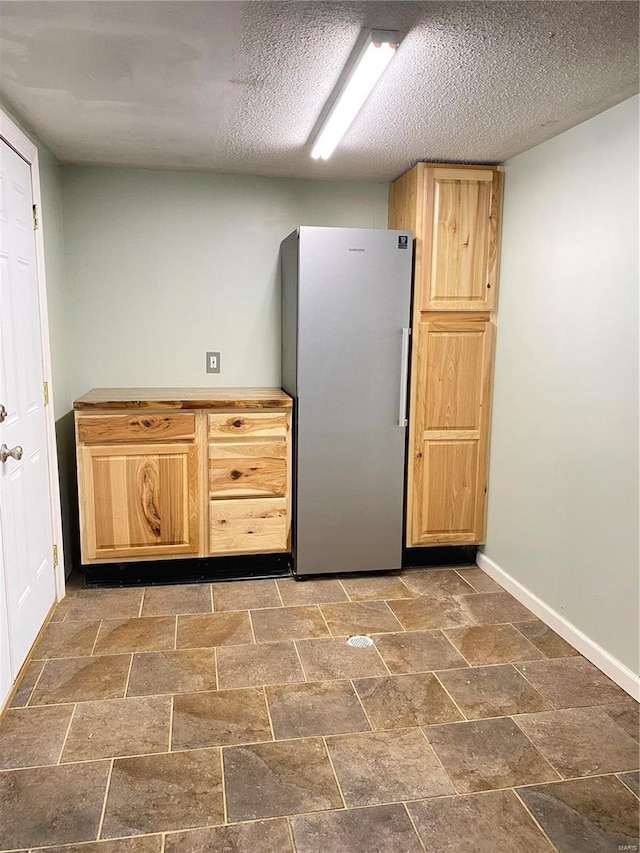 kitchen featuring stainless steel refrigerator, a textured ceiling, and light brown cabinets