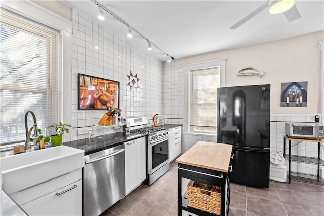 kitchen with appliances with stainless steel finishes, white cabinetry, tile patterned floors, sink, and tile walls