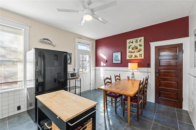 dining space featuring dark tile patterned flooring, tile walls, and ceiling fan