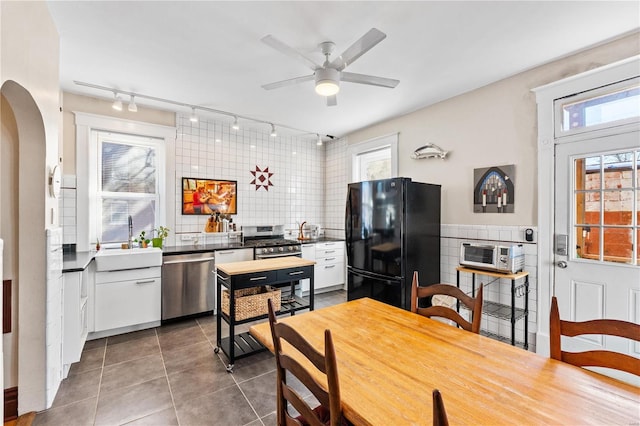 kitchen with dark tile patterned flooring, white cabinetry, sink, black fridge, and stainless steel dishwasher