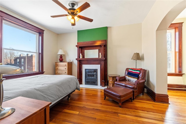 bedroom with ceiling fan, a brick fireplace, and hardwood / wood-style floors