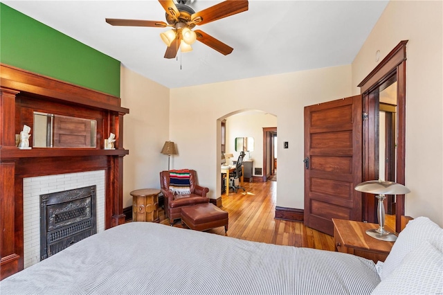 bedroom featuring ceiling fan, light hardwood / wood-style floors, and a brick fireplace