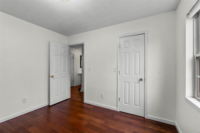 unfurnished bedroom featuring dark wood-type flooring, multiple windows, and a textured ceiling