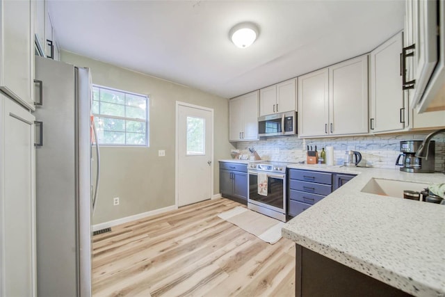 kitchen featuring light hardwood / wood-style flooring, white cabinetry, appliances with stainless steel finishes, light stone counters, and tasteful backsplash