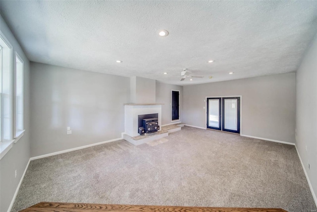 unfurnished living room featuring carpet, ceiling fan, a wood stove, and a textured ceiling