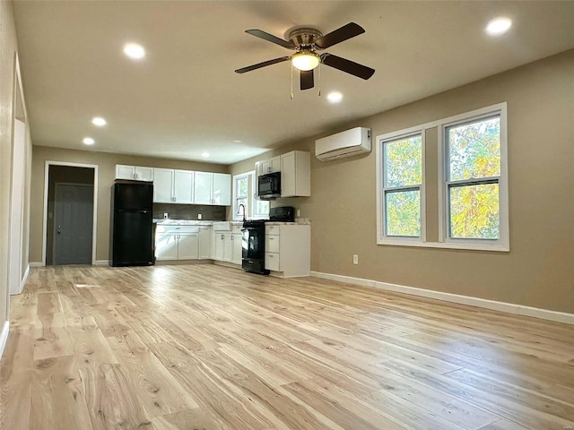 kitchen featuring white cabinetry, a wall unit AC, black appliances, and light hardwood / wood-style flooring