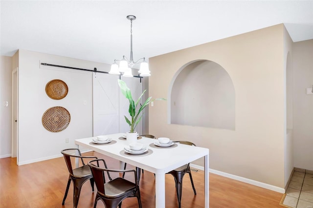 dining space with hardwood / wood-style flooring, a barn door, and an inviting chandelier