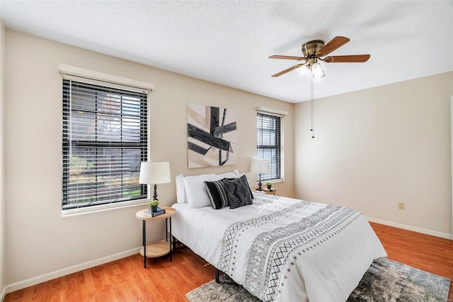 bedroom featuring wood-type flooring, a textured ceiling, multiple windows, and ceiling fan