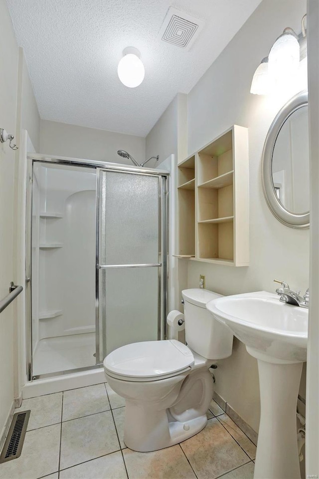 bathroom with tile patterned floors, toilet, a shower with door, and a textured ceiling