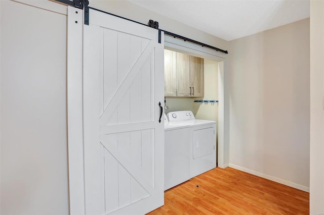 clothes washing area featuring cabinets, a barn door, light hardwood / wood-style floors, a textured ceiling, and washer and dryer