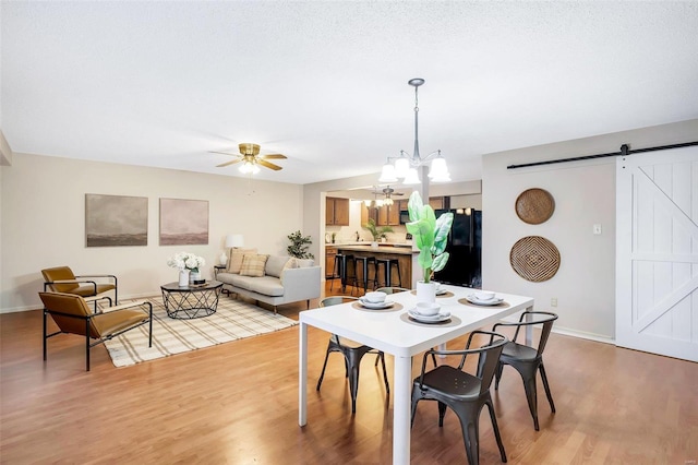 dining room with a barn door, light hardwood / wood-style flooring, and ceiling fan with notable chandelier