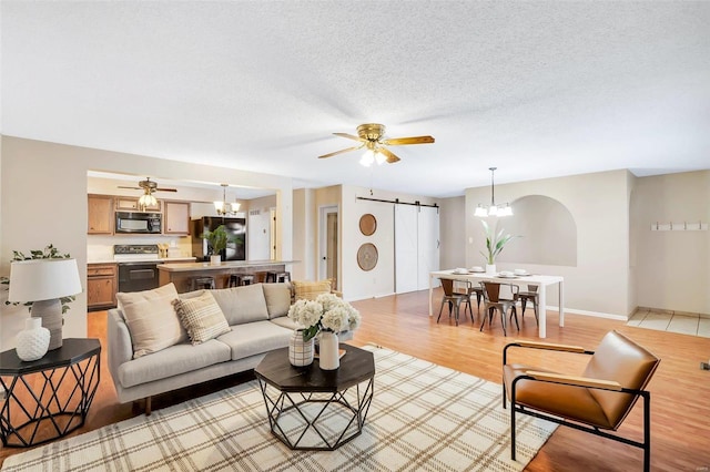 living room featuring ceiling fan with notable chandelier, a textured ceiling, a barn door, and light hardwood / wood-style floors