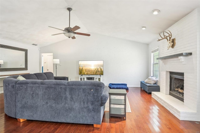 living room with hardwood / wood-style flooring, ceiling fan, a fireplace, and vaulted ceiling