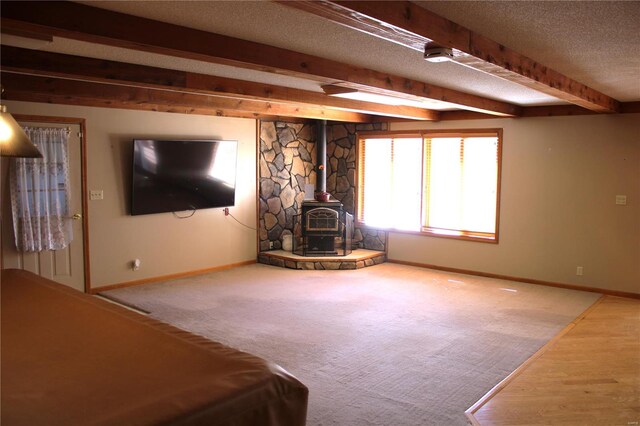 unfurnished living room featuring beam ceiling, a wood stove, a textured ceiling, and carpet floors