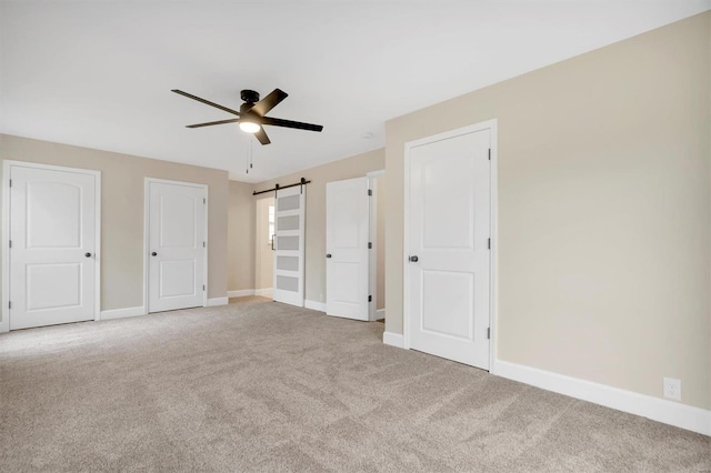 unfurnished bedroom with light colored carpet, a barn door, and ceiling fan