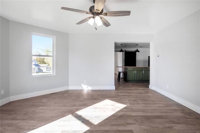 empty room with a barn door, wood-type flooring, and ceiling fan