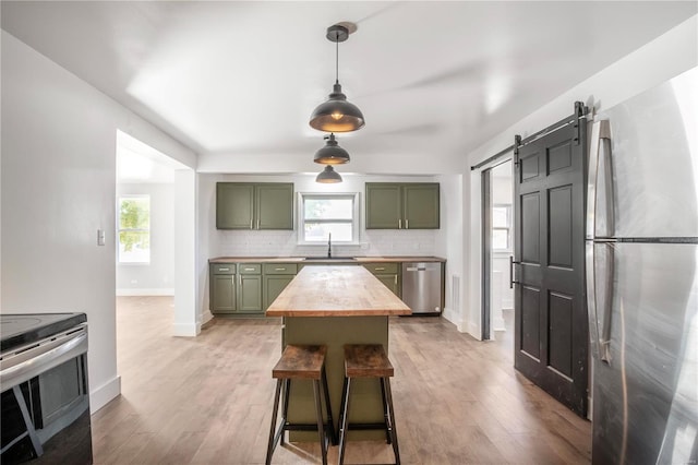 kitchen with a barn door, green cabinetry, stainless steel appliances, and a wealth of natural light