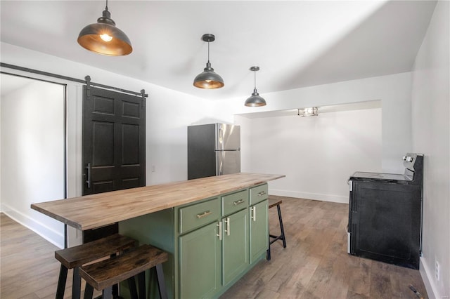 kitchen with a barn door, stove, stainless steel refrigerator, green cabinets, and butcher block countertops