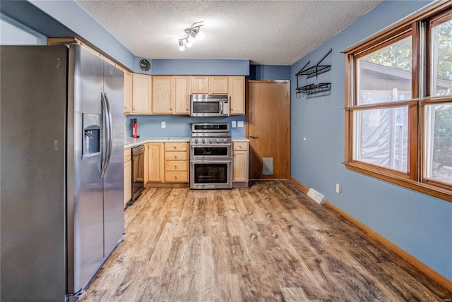 kitchen featuring light brown cabinetry, stainless steel appliances, a textured ceiling, and light hardwood / wood-style flooring