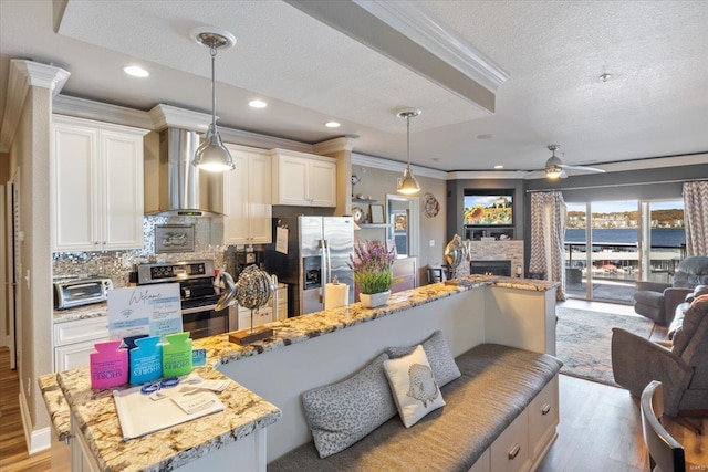 kitchen with light hardwood / wood-style flooring, wall chimney exhaust hood, ceiling fan, appliances with stainless steel finishes, and decorative light fixtures