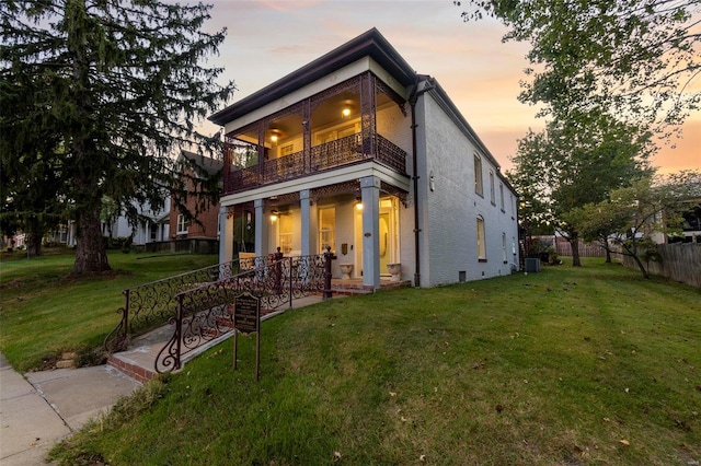 back house at dusk featuring central AC, a lawn, and a balcony