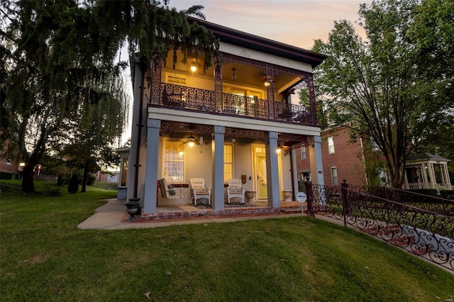 back house at dusk featuring a patio area, a lawn, a balcony, and ceiling fan