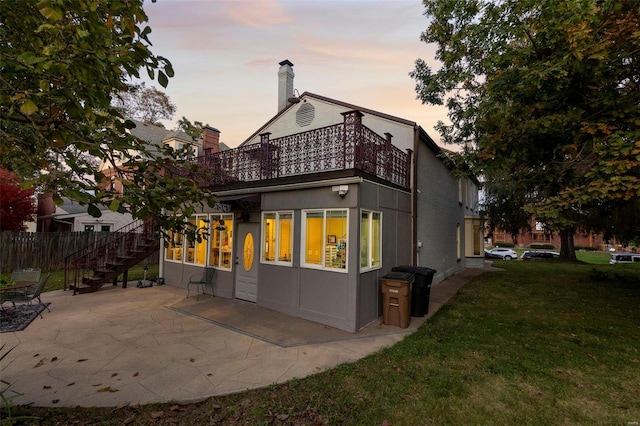 back house at dusk featuring a patio area and a lawn