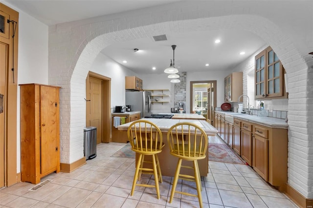 kitchen with a kitchen island, a breakfast bar area, sink, stainless steel refrigerator with ice dispenser, and decorative light fixtures