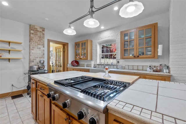 kitchen with hanging light fixtures, light tile patterned floors, tile countertops, stainless steel gas cooktop, and sink