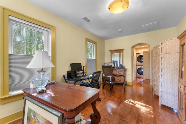 office space with a healthy amount of sunlight, stacked washer and clothes dryer, and dark hardwood / wood-style flooring