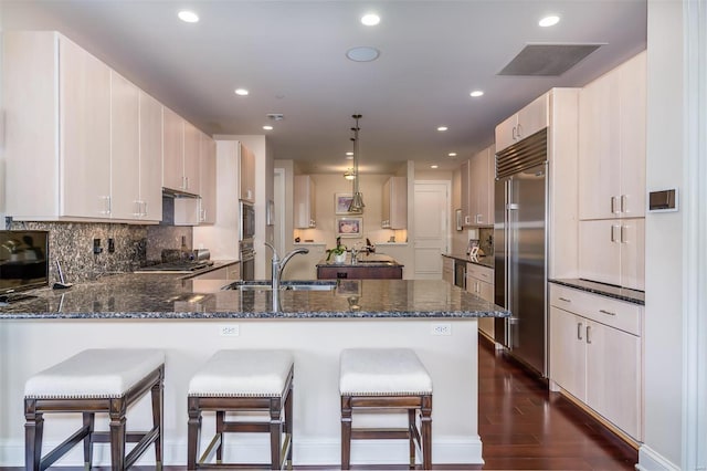 kitchen with dark wood-type flooring, built in appliances, kitchen peninsula, sink, and pendant lighting