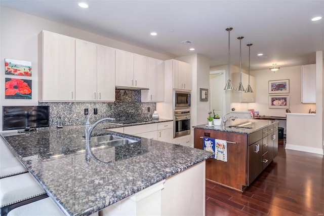 kitchen featuring stainless steel oven, dark hardwood / wood-style floors, sink, built in microwave, and decorative light fixtures