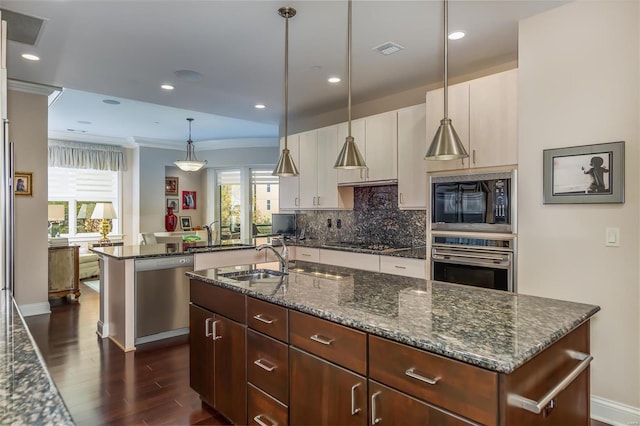 kitchen with appliances with stainless steel finishes, sink, pendant lighting, and a kitchen island with sink