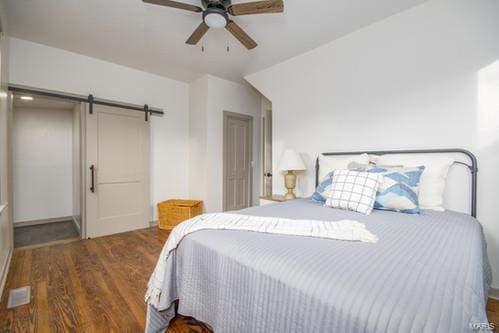 bedroom with ceiling fan, dark hardwood / wood-style floors, vaulted ceiling, and a barn door