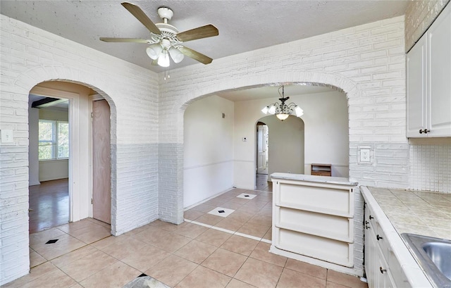 kitchen featuring tile countertops, brick wall, white cabinets, and hanging light fixtures