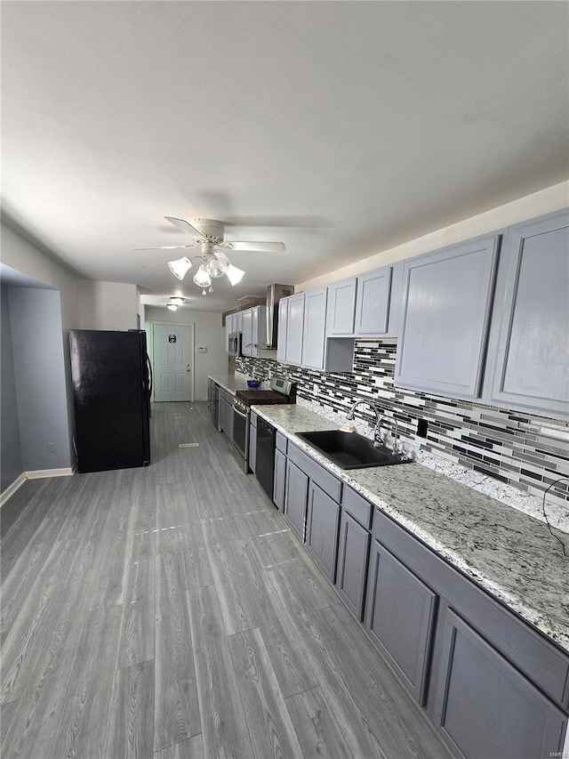 kitchen with tasteful backsplash, light wood finished floors, gray cabinets, black appliances, and a sink