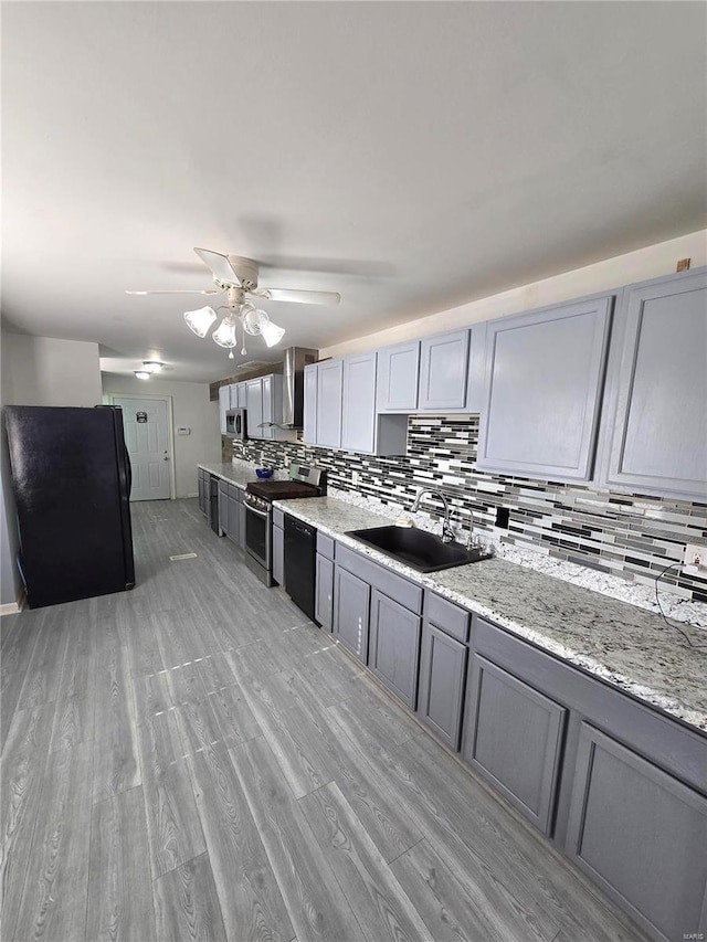 kitchen featuring black appliances, gray cabinets, a sink, backsplash, and wall chimney range hood