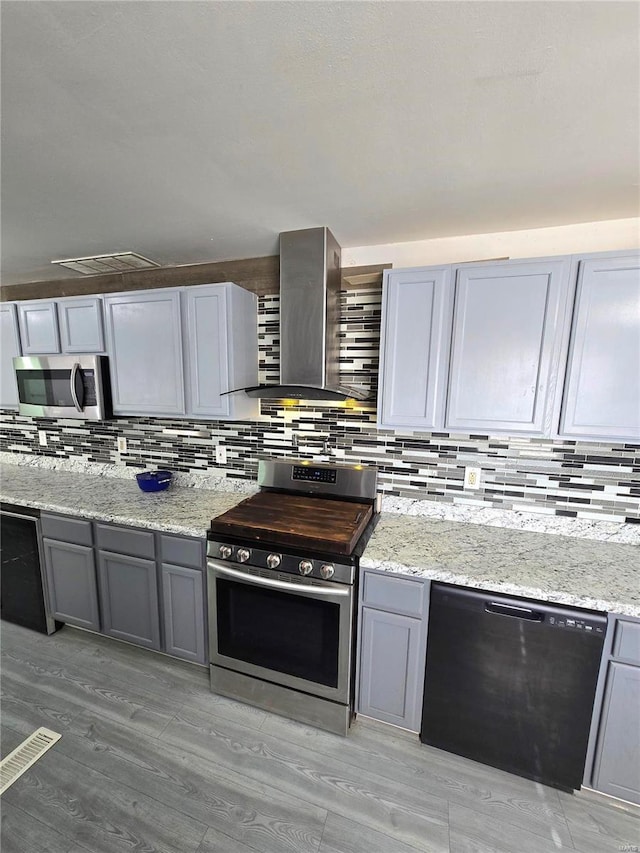 kitchen with tasteful backsplash, gray cabinets, stainless steel appliances, and wall chimney exhaust hood