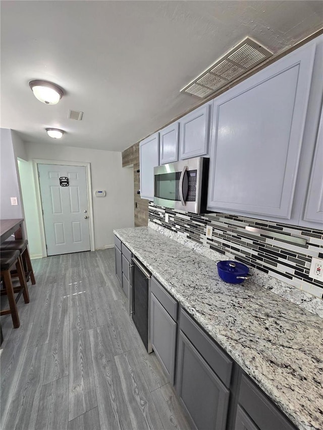 kitchen featuring visible vents, gray cabinetry, stainless steel microwave, backsplash, and light wood-style floors