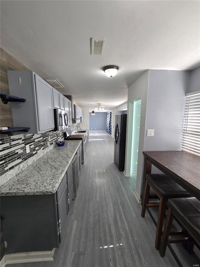 kitchen featuring light stone counters, dark wood-style floors, visible vents, decorative backsplash, and appliances with stainless steel finishes