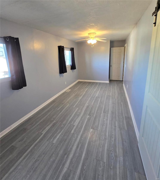 unfurnished room with visible vents, wood finished floors, a barn door, baseboards, and ceiling fan