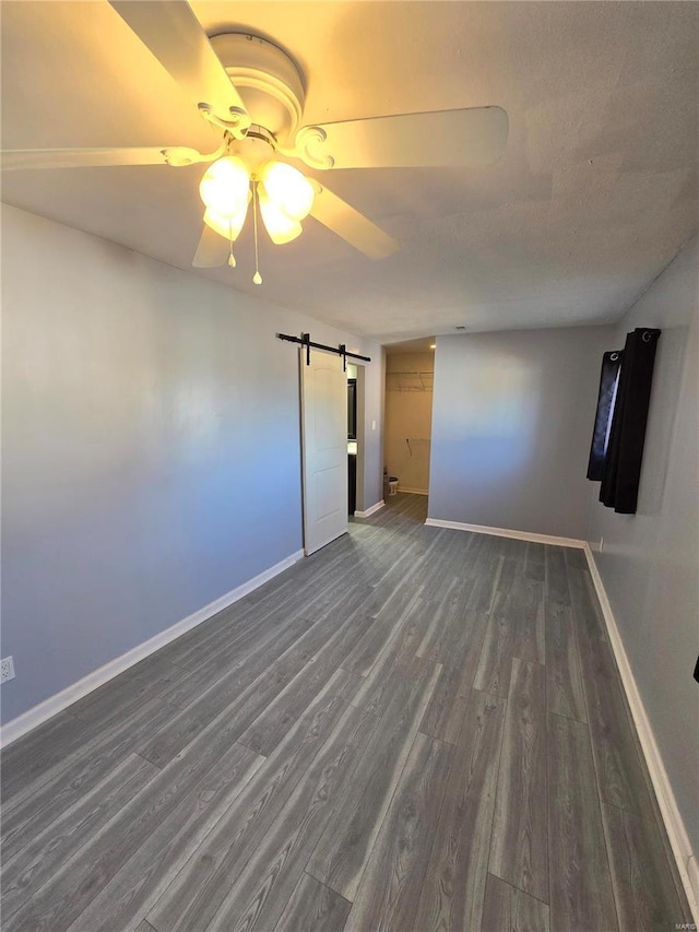 unfurnished room with dark wood finished floors, a barn door, a ceiling fan, and baseboards