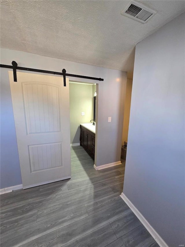 corridor featuring visible vents, baseboards, a barn door, a textured ceiling, and dark wood-style flooring