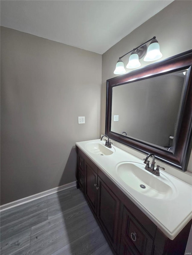 bathroom with a sink, baseboards, wood finished floors, and double vanity